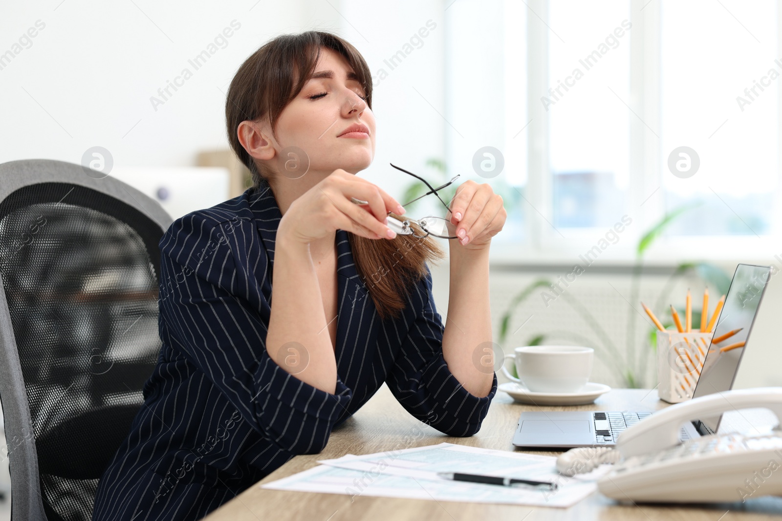 Photo of Overwhelmed office worker sitting at table with laptop and documents indoors