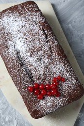 Tasty chocolate sponge cake with powdered sugar and currant on light grey textured table, top view