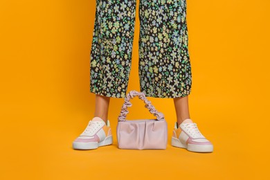 Woman with stylish bag on yellow background, closeup