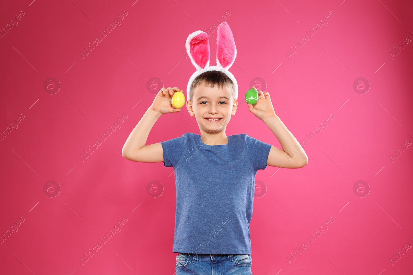 Photo of Little boy in bunny ears headband holding Easter eggs on color background