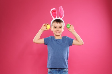 Photo of Little boy in bunny ears headband holding Easter eggs on color background