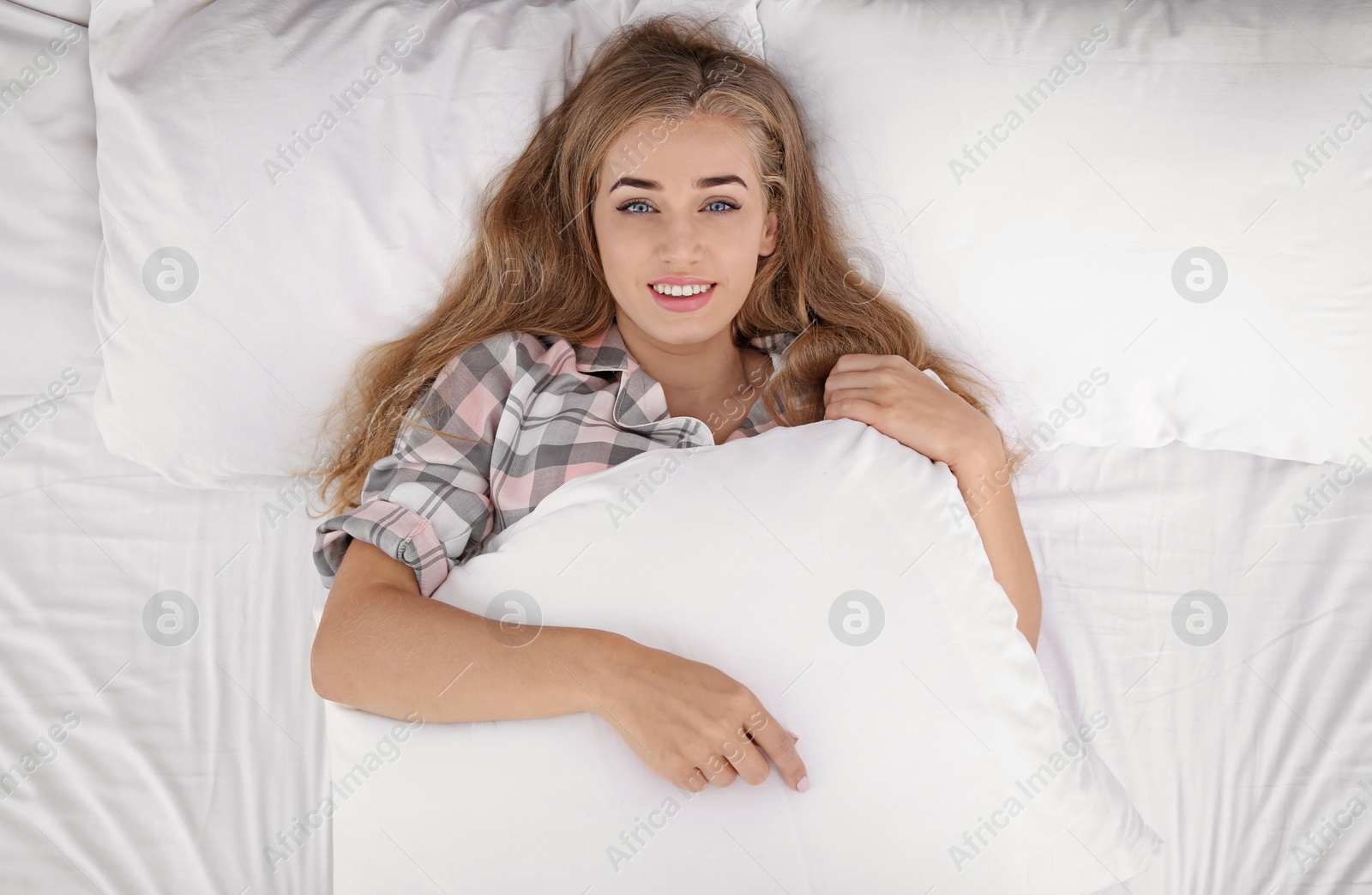 Photo of Beautiful young woman lying with comfortable pillow in bed, top view