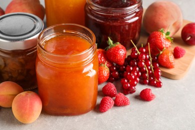 Jars with different jams and fresh fruits on grey table