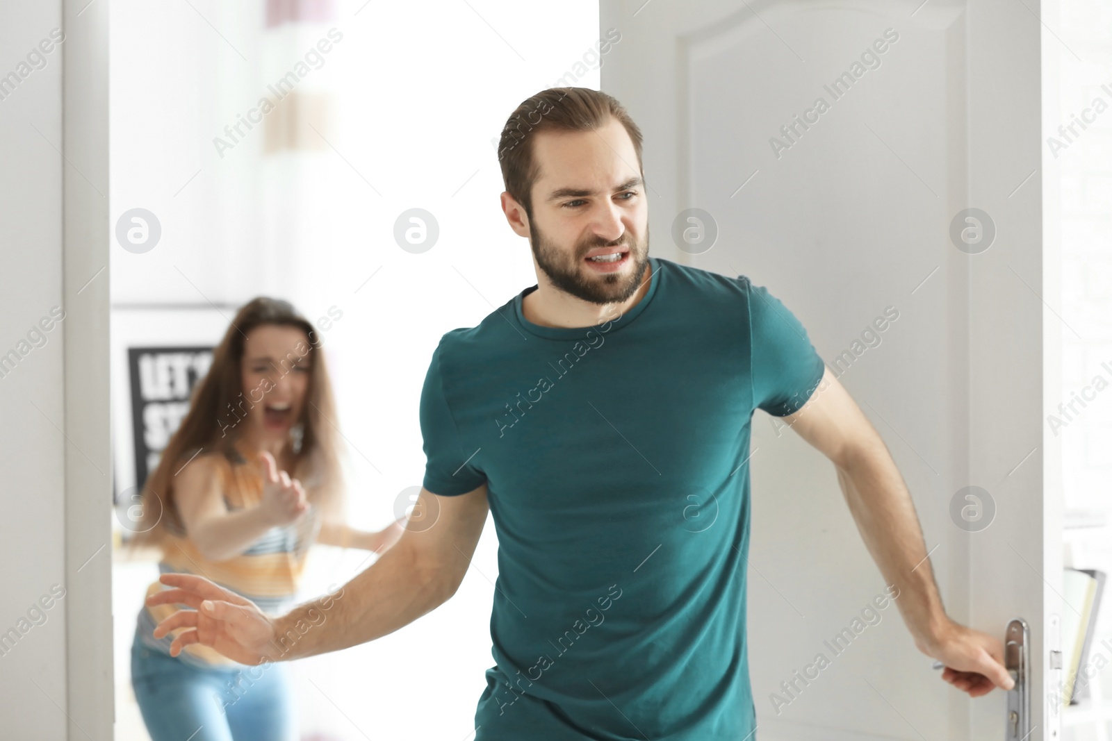 Photo of Young man walking out of door during argument with his girlfriend indoors