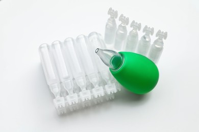Photo of Single dose ampoules of sterile isotonic sea water solution and nasal aspirator on white background