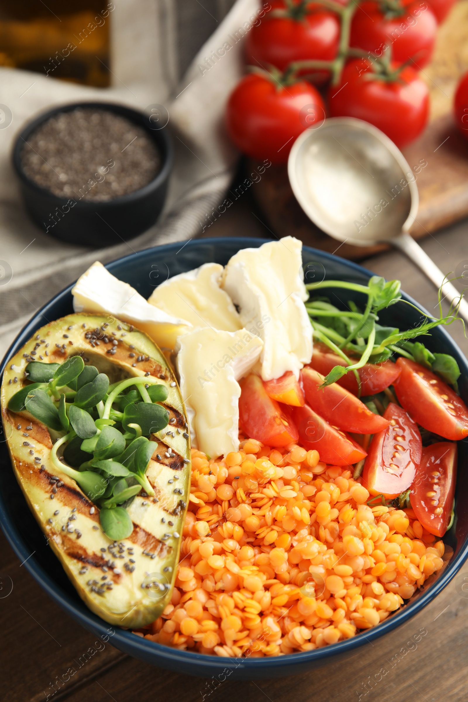 Photo of Delicious lentil bowl with soft cheese, avocado and tomatoes on wooden table