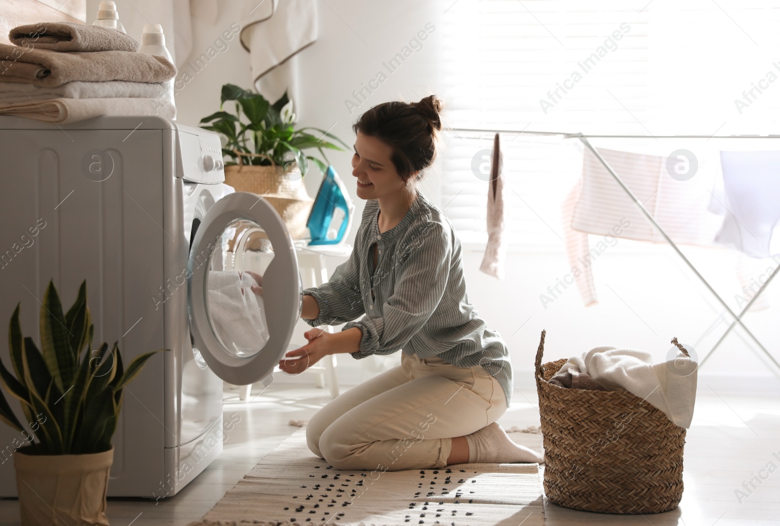 Photo of Young woman taking laundry out of washing machine at home