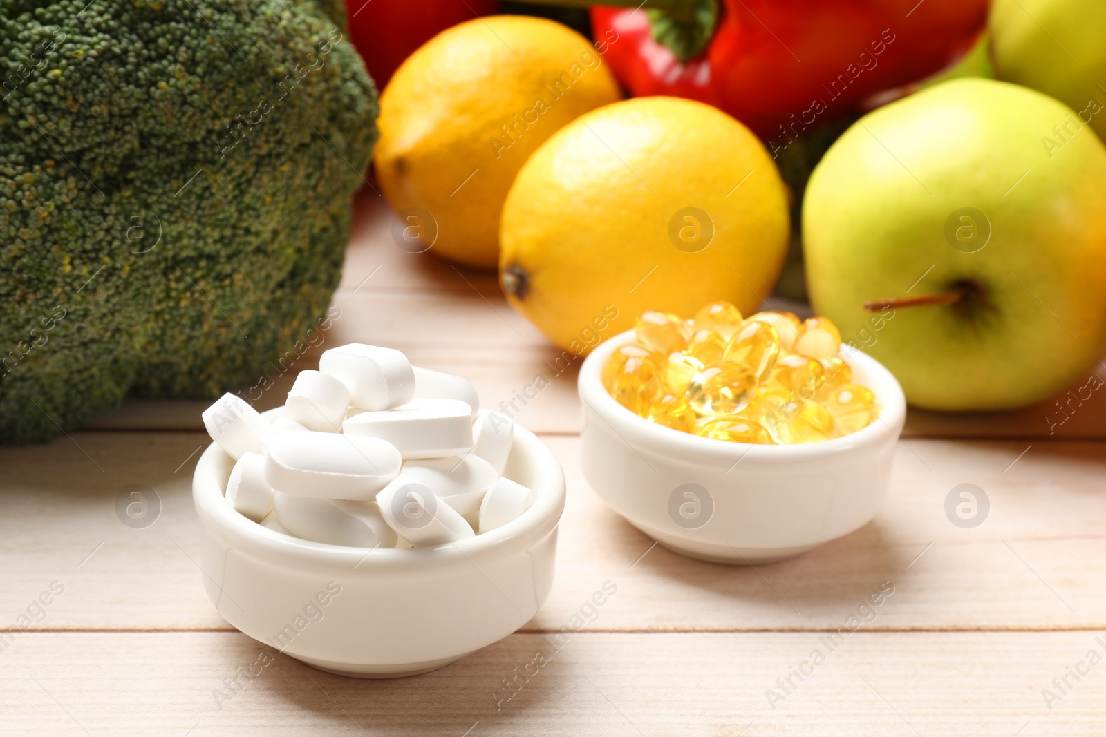 Photo of Dietary supplements. Bowls with different pills near food products on light wooden table, closeup