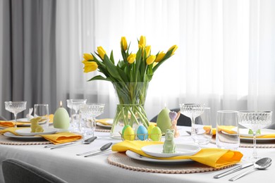 Photo of Festive table setting with glasses, painted eggs and vase of tulips. Easter celebration