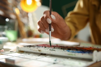 Photo of Young woman drawing with watercolors at table, closeup