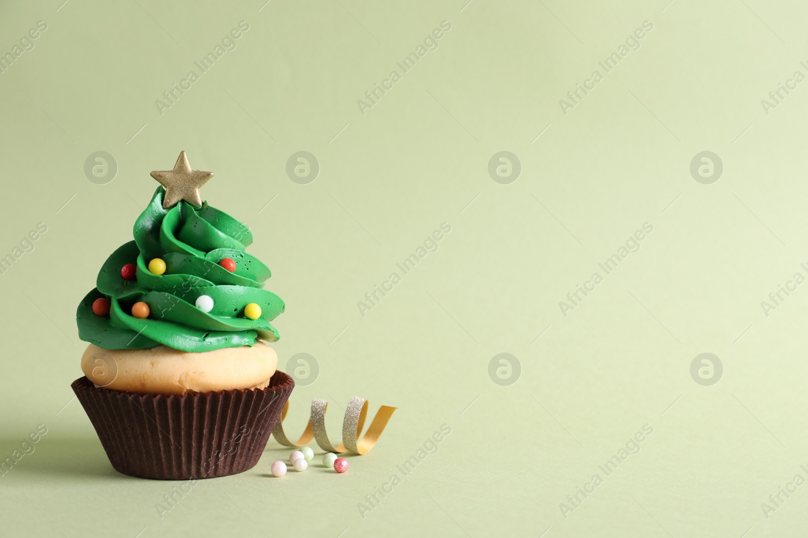 Photo of Christmas tree shaped cupcake and streamer on green background. Space for text