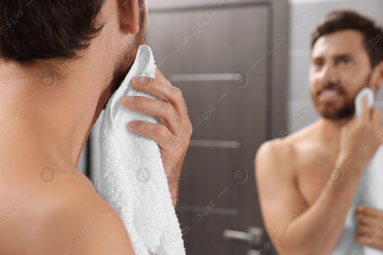 Photo of Handsome man with towel in front of mirror in bathroom