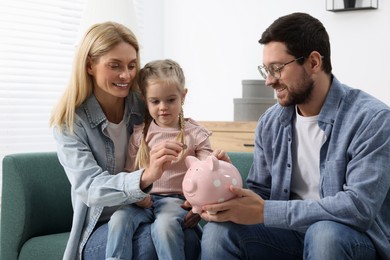Planning budget together. Little girl with her parents putting coins into piggybank at home