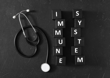 Photo of Cubes with words Immune System and stethoscope on black table, flat lay