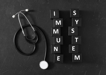 Cubes with words Immune System and stethoscope on black table, flat lay