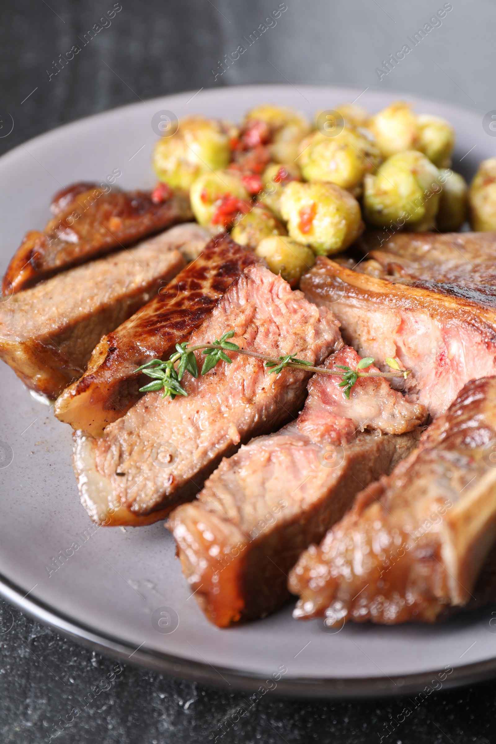 Photo of Delicious fried beef meat, vegetables and thyme on black table, closeup