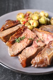 Delicious fried beef meat, vegetables and thyme on black table, closeup