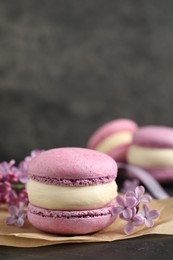 Photo of Delicious violet macaron and lilac flowers on black table, closeup. Space for text