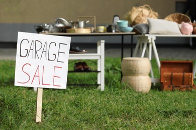 Photo of Sign Garage sale written on cardboard near tables with different stuff in yard