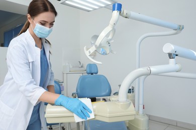 Photo of Professional dentist in white coat and medical mask cleaning workplace indoors