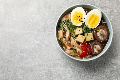 Photo of Bowl of delicious ramen on grey table, top view with space for text. Noodle soup