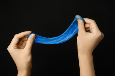 Woman playing with blue slime on black background, closeup. Antistress toy