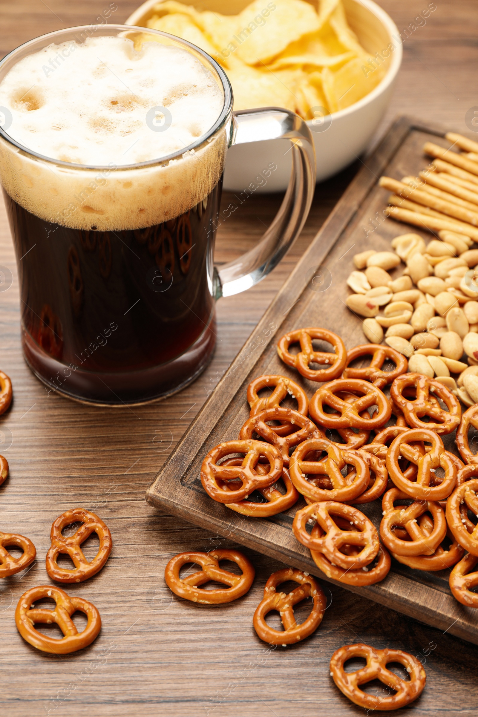 Photo of Glass of beer served with delicious pretzel crackers and other snacks on wooden table