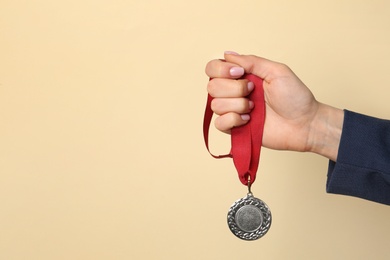 Photo of Woman holding golden medal on color background, closeup. Space for text