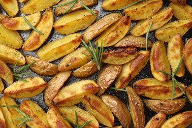 Photo of Delicious baked potatoes with rosemary on black surface, flat lay