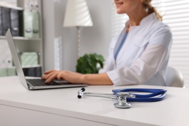 Photo of Doctor with laptop and stethoscope at white table, closeup. Patient consultation