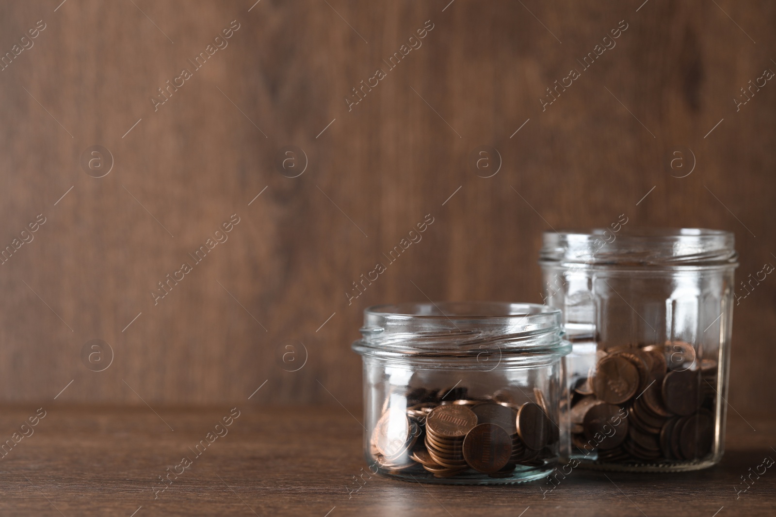 Photo of Glass jars with coins on wooden table. Space for text