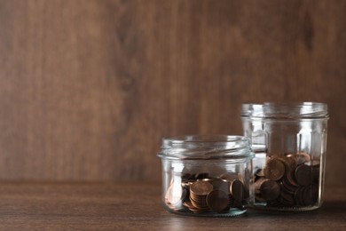 Glass jars with coins on wooden table. Space for text