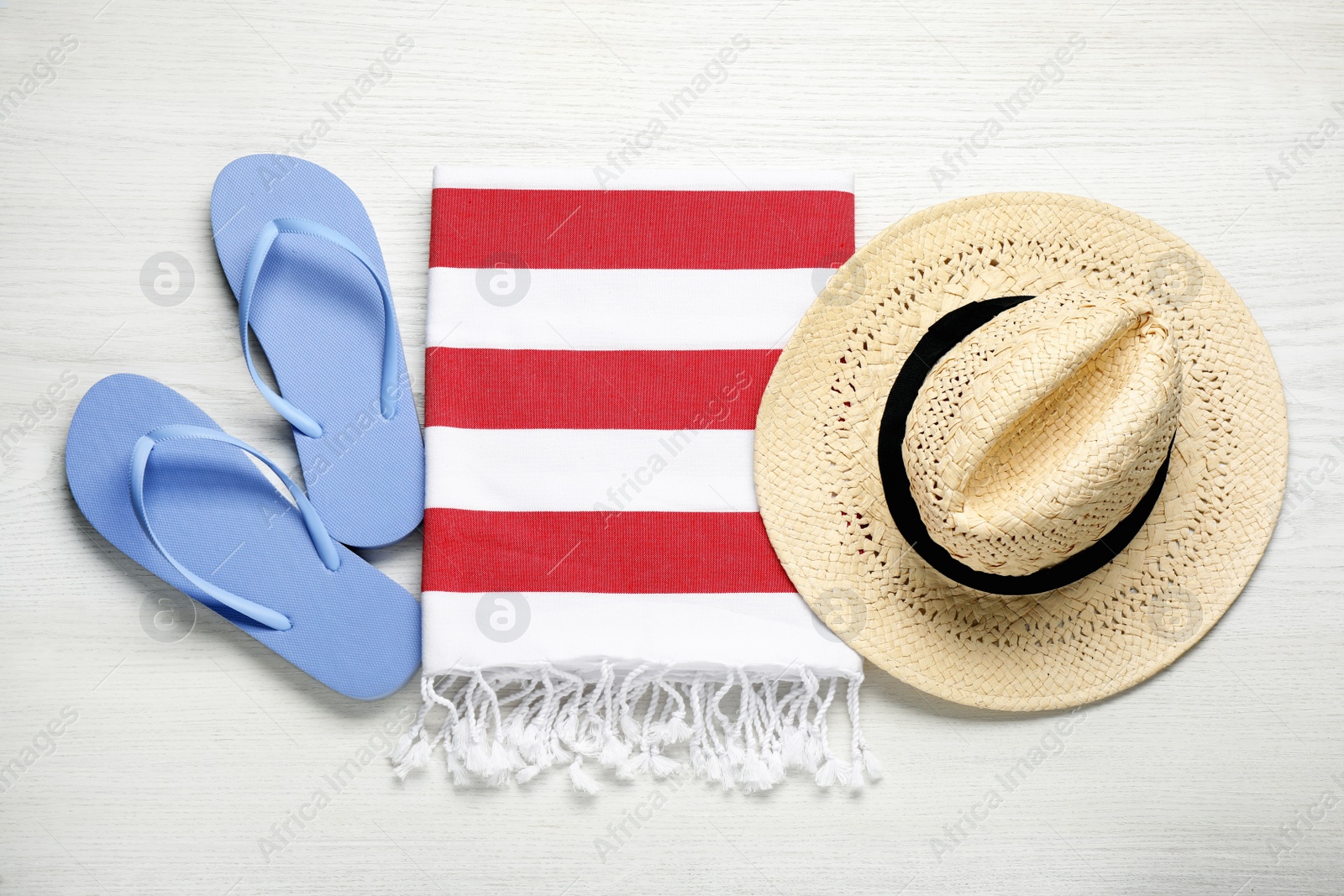 Photo of Beach towel, flip flops and straw hat on white wooden background, flat lay