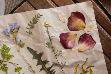 Photo of Sheet of paper with dried flowers and leaves on wooden table, top view