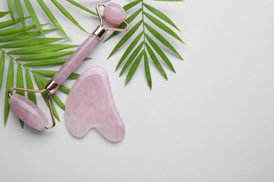 Photo of Gua sha stone, face roller and green leaves on light background, flat lay. Space for text