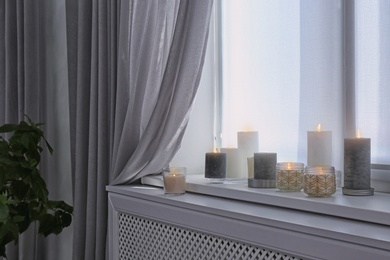 Photo of Burning candles on window sill in room