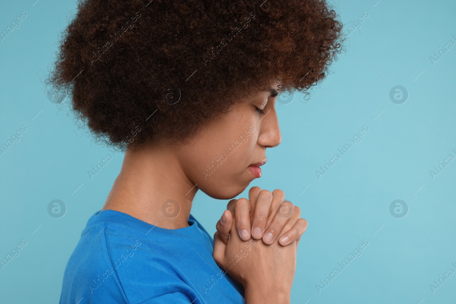 Photo of Woman with clasped hands praying to God on light blue background