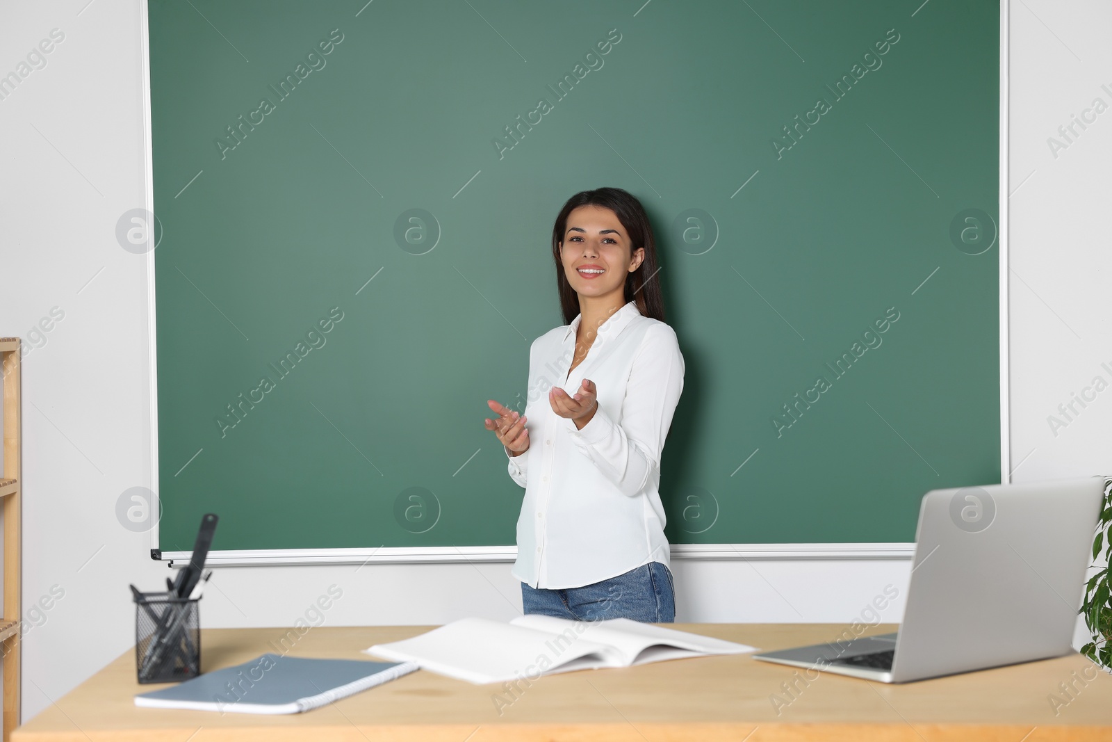 Photo of Happy young teacher giving lesson at blackboard in classroom. Space for text
