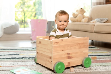 Photo of Adorable little baby in wooden cart at home