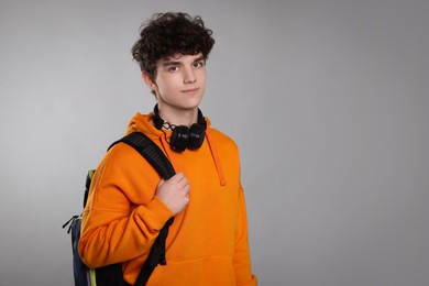 Teenage boy with headphones and backpack on light grey background. Space for text