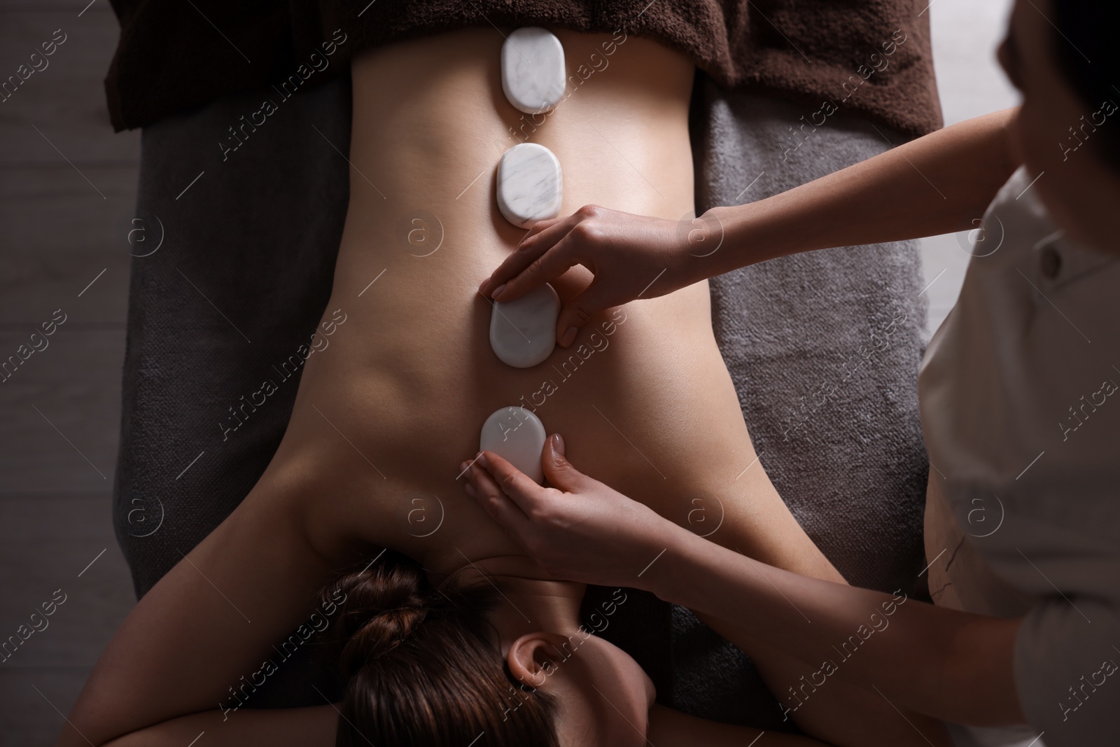 Photo of Spa therapy. Beautiful young woman lying on table during hot stone massage in salon, top view