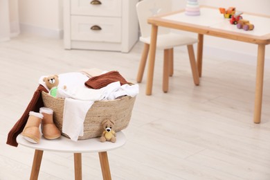 Photo of Laundry basket with baby clothes, shoes and crochet toys on white wooden table in child room, space for text