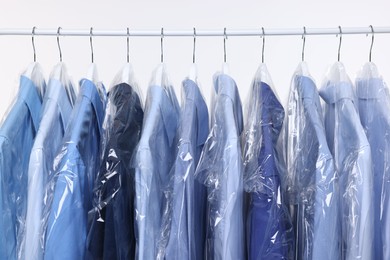 Dry-cleaning service. Many different clothes in plastic bags hanging on rack against white background, closeup