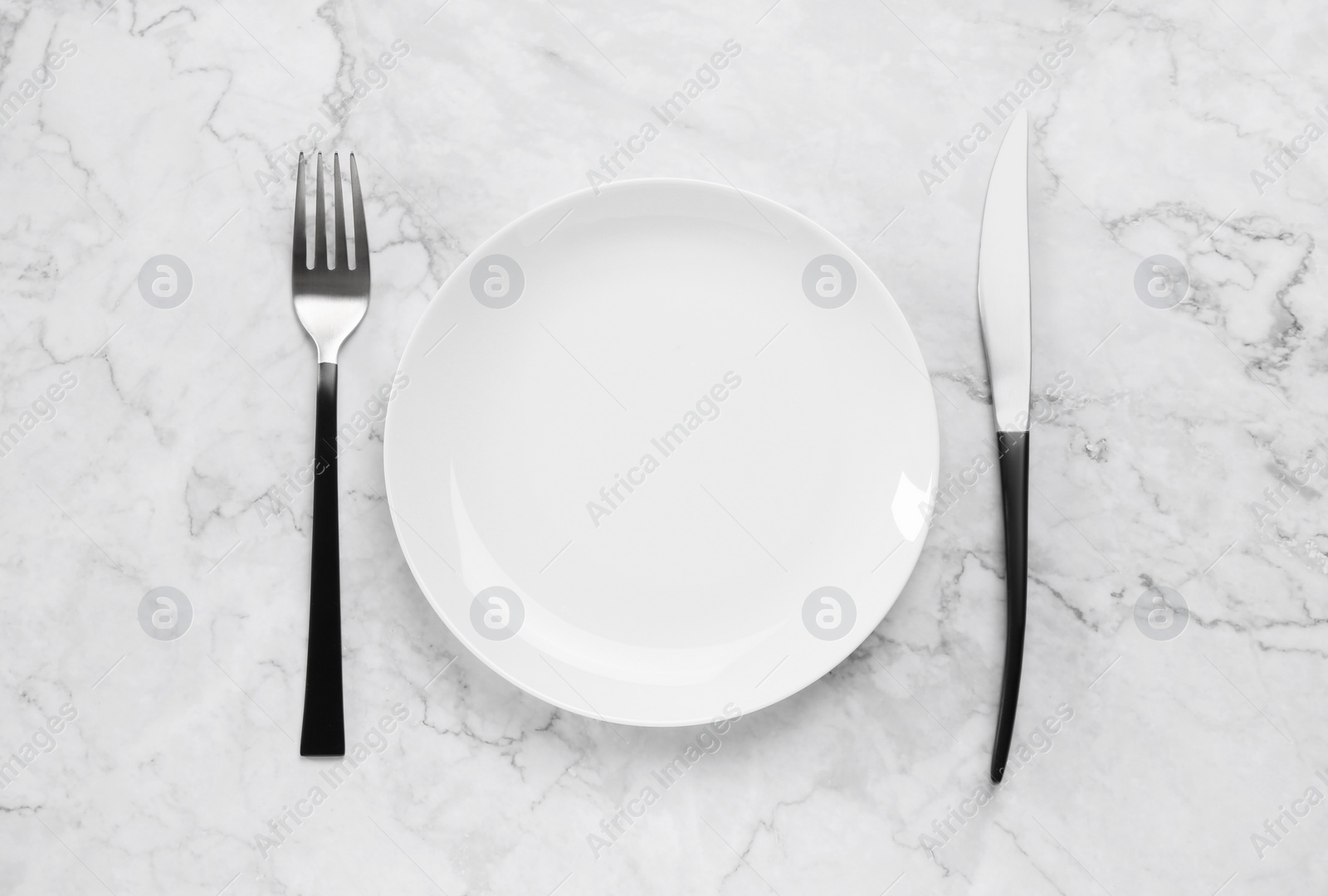 Photo of Clean plate and shiny silver cutlery on white marble table, flat lay