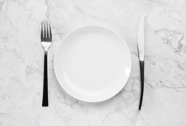 Photo of Clean plate and shiny silver cutlery on white marble table, flat lay