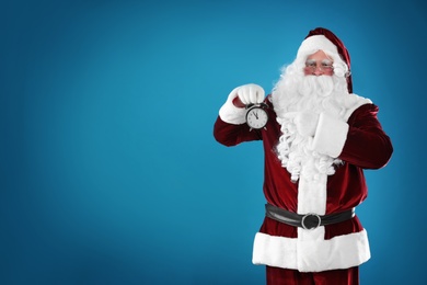 Photo of Santa Claus holding alarm clock on blue background, space for text. Christmas countdown