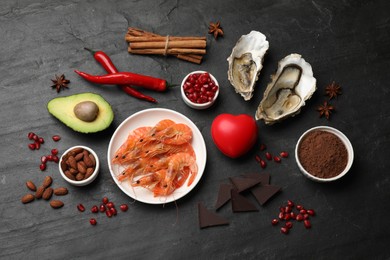 Photo of Natural aphrodisiac. Different food products and heart model on black table, flat lay