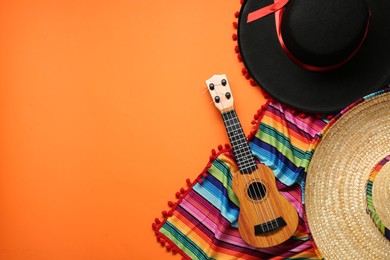 Mexican sombrero hats, guitar and colorful poncho on orange background, flat lay. Space for text