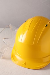 Hard hat and goggles on white table, closeup. Safety equipment