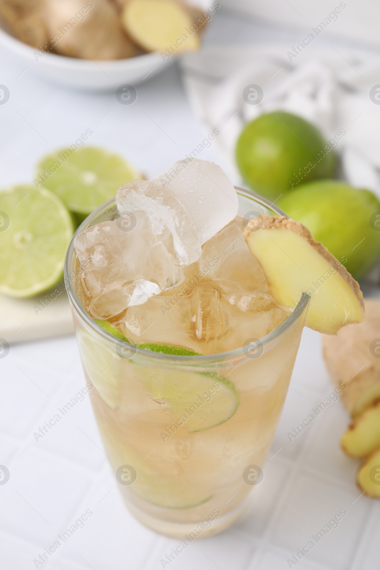 Photo of Glass of tasty ginger ale with ice cubes and ingredients on white tiled table, closeup